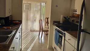 A kitchen with white cabinets, a refrigerator, a stove, and a sink. There is a chair and a window with blinds. - Ferienvilla Bell Villa Bonita Springs (Bonita Springs)