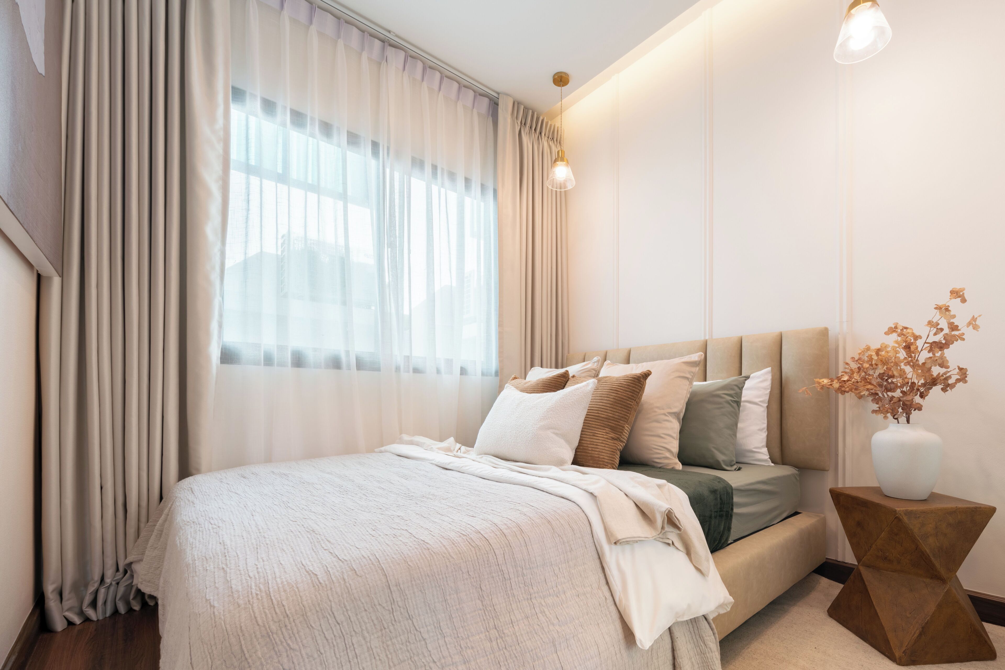 A modern bedroom with a bed, curtains, a bedside lamp, and a vase with dried flowers.