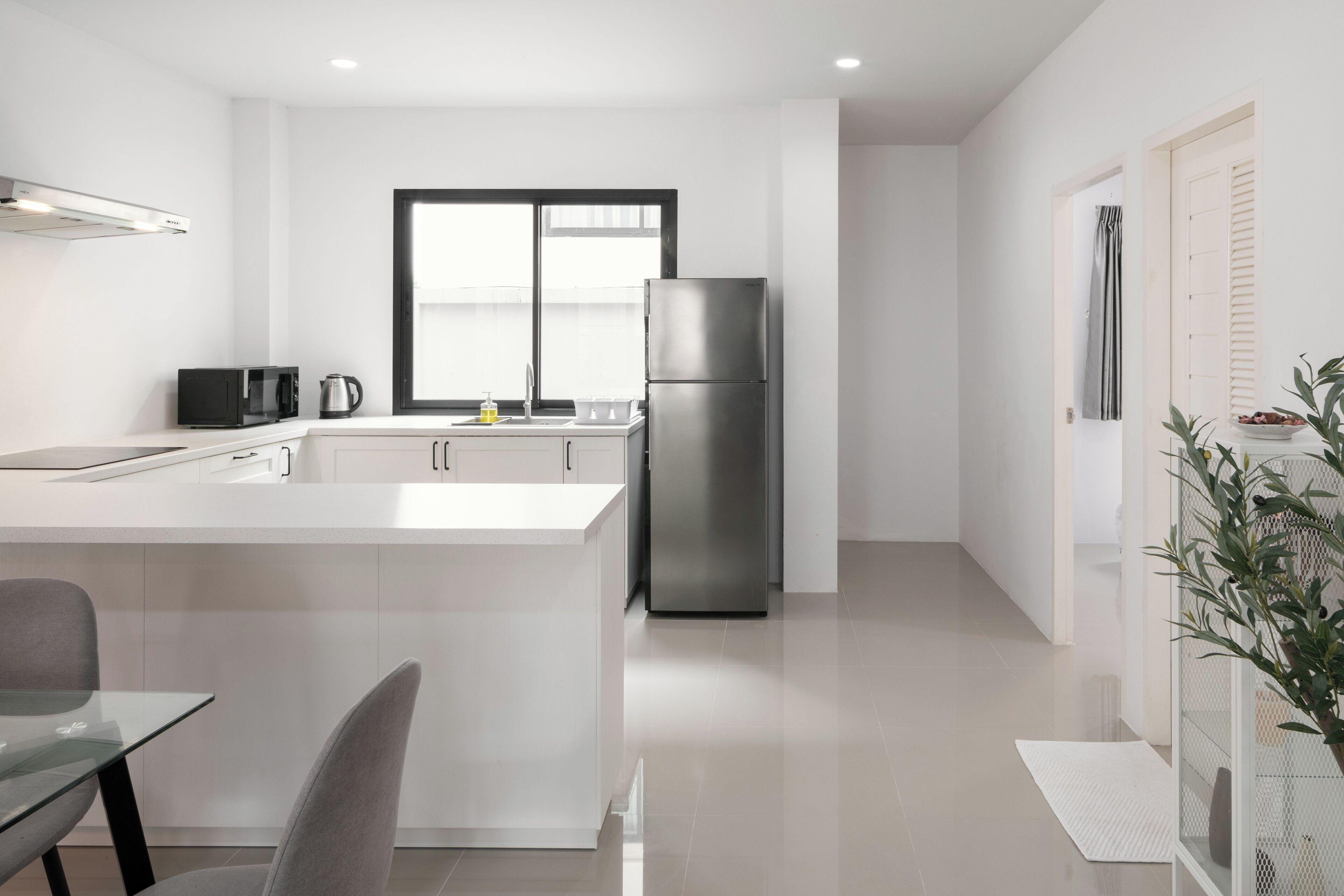Une cuisine moderne dotée d’un grand îlot central, d’appareils électroménagers en acier inoxydable et offrant une vue sur l’extérieur.