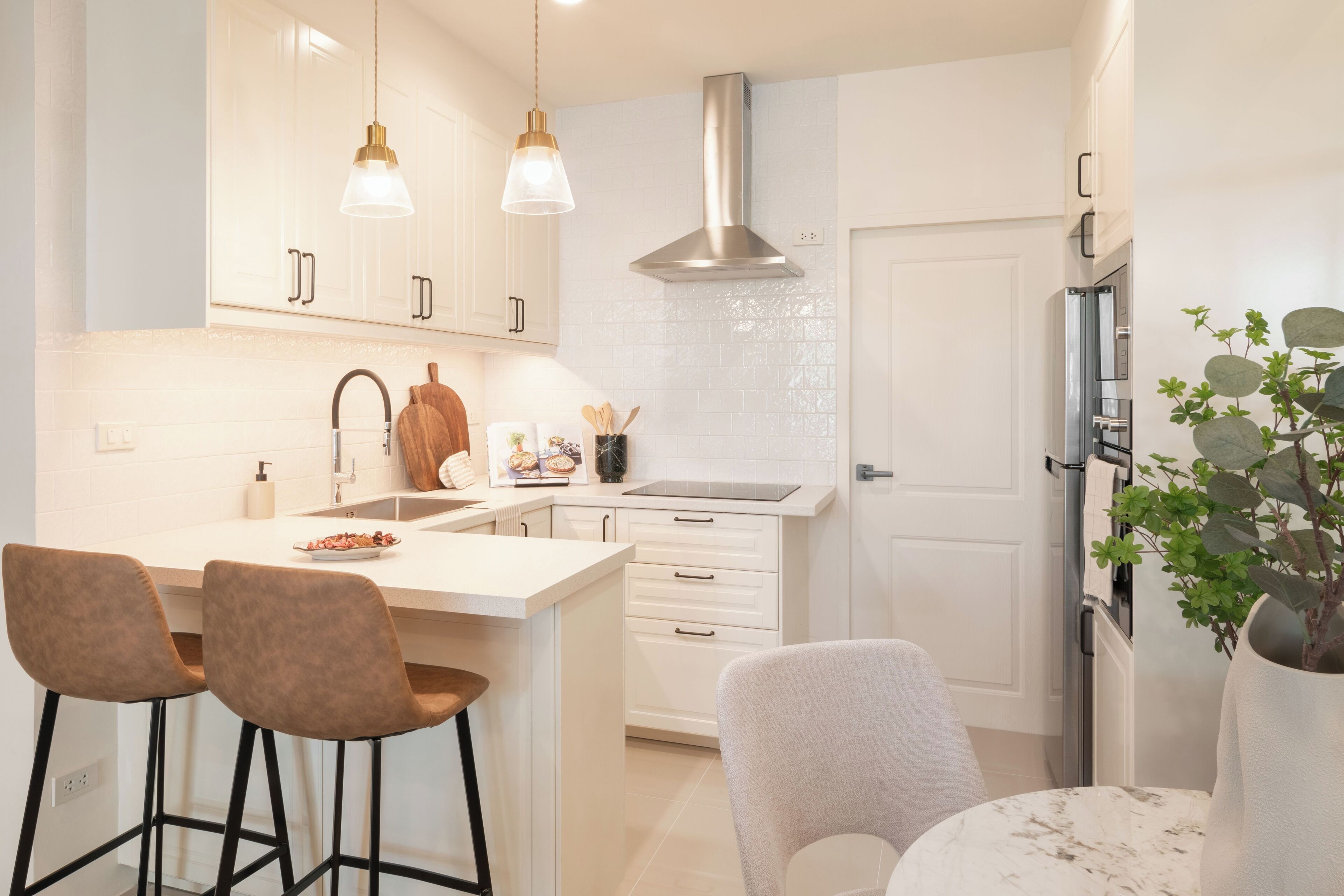 A modern kitchen with white cabinetry, a central island with stools, a stainless steel range hood, and a refrigerator.