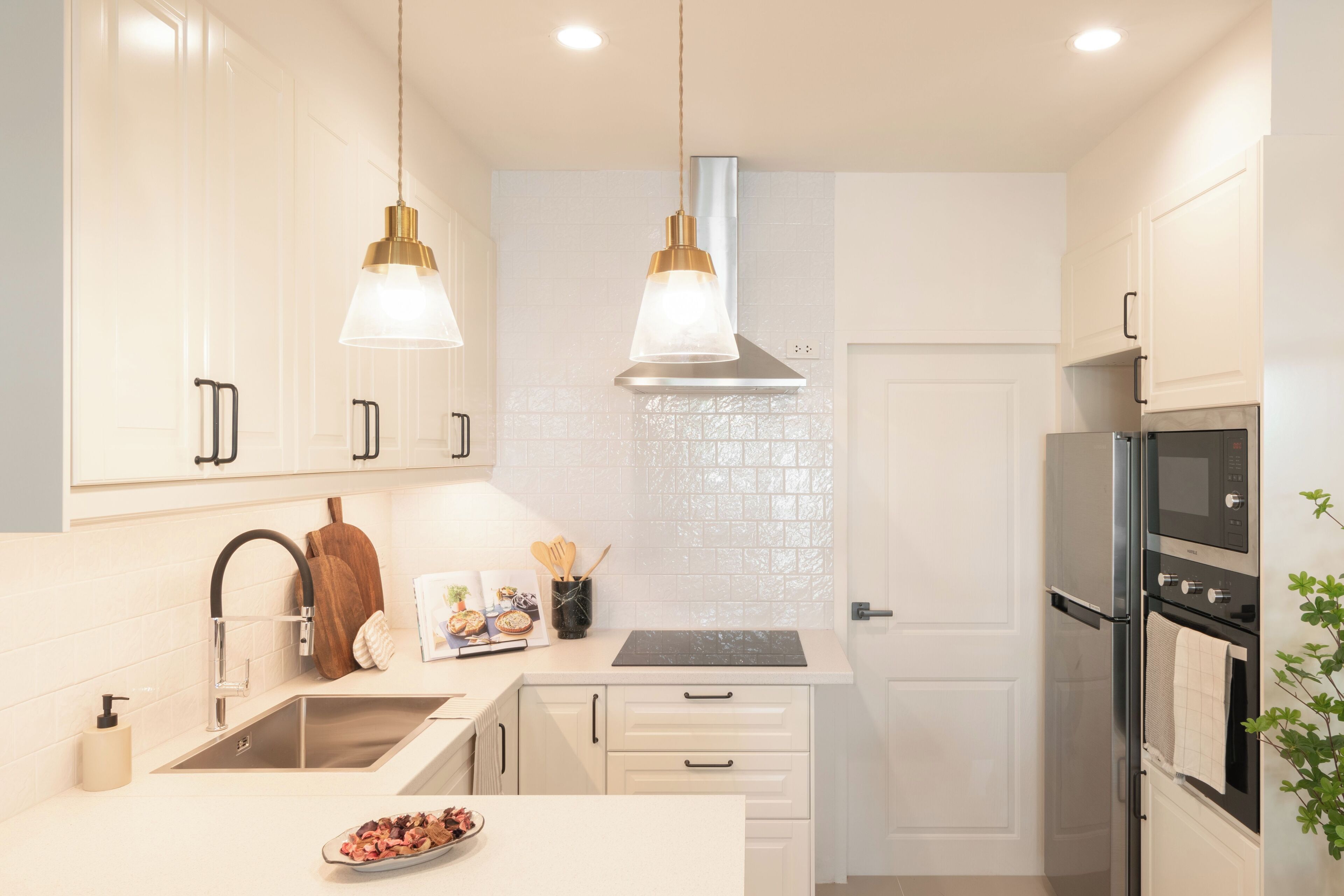 Une cuisine moderne avec des armoires blanches, des appareils en acier inoxydable et des luminaires suspendus.