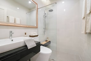 A modern bathroom with a glass-enclosed shower, a white sink, and a black countertop. - Chao Wilai Residence | Naiyang Beach | HKT Airport (Sa Khu)