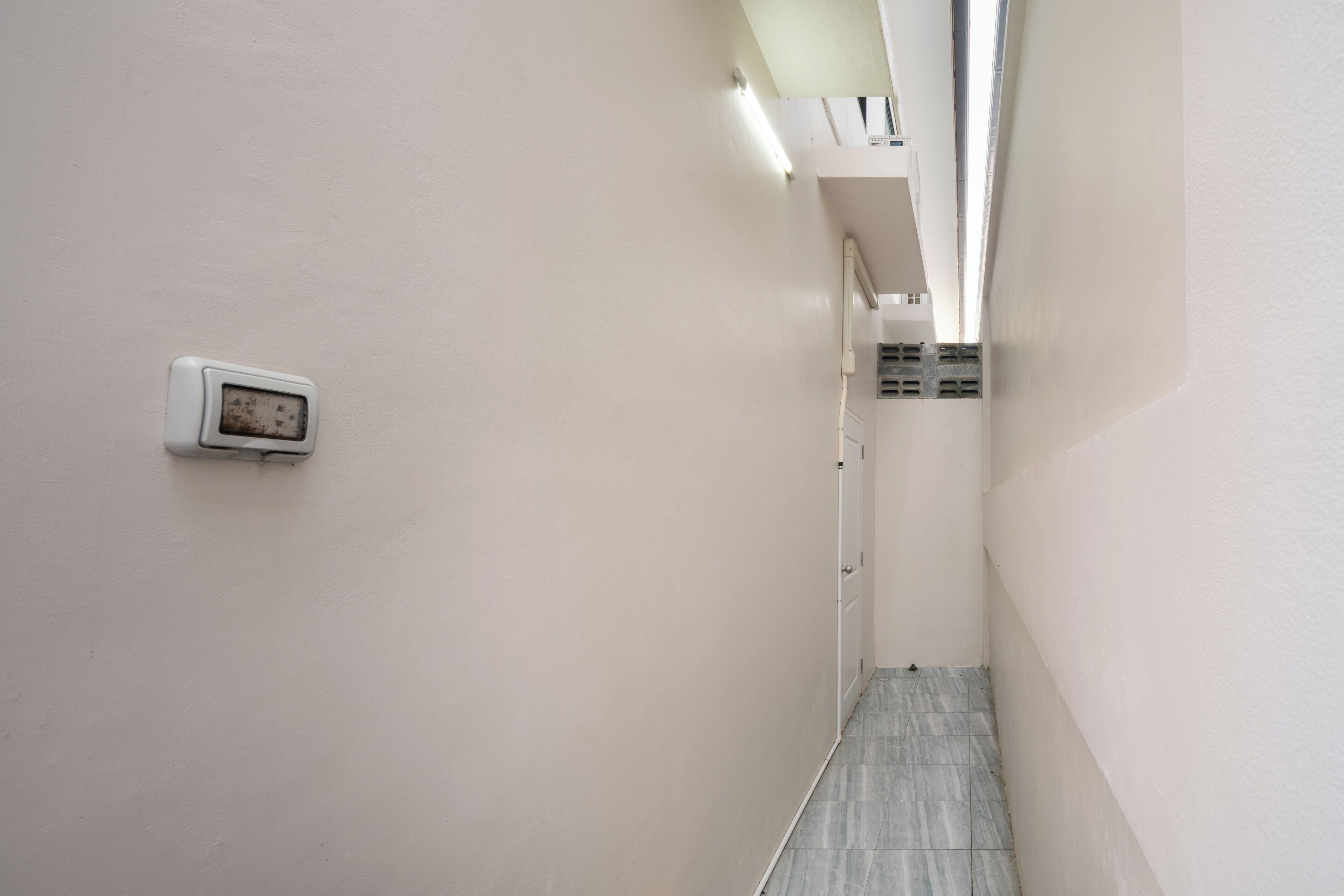 Un couloir étroit, avec un thermostat au mur et une porte au bout.