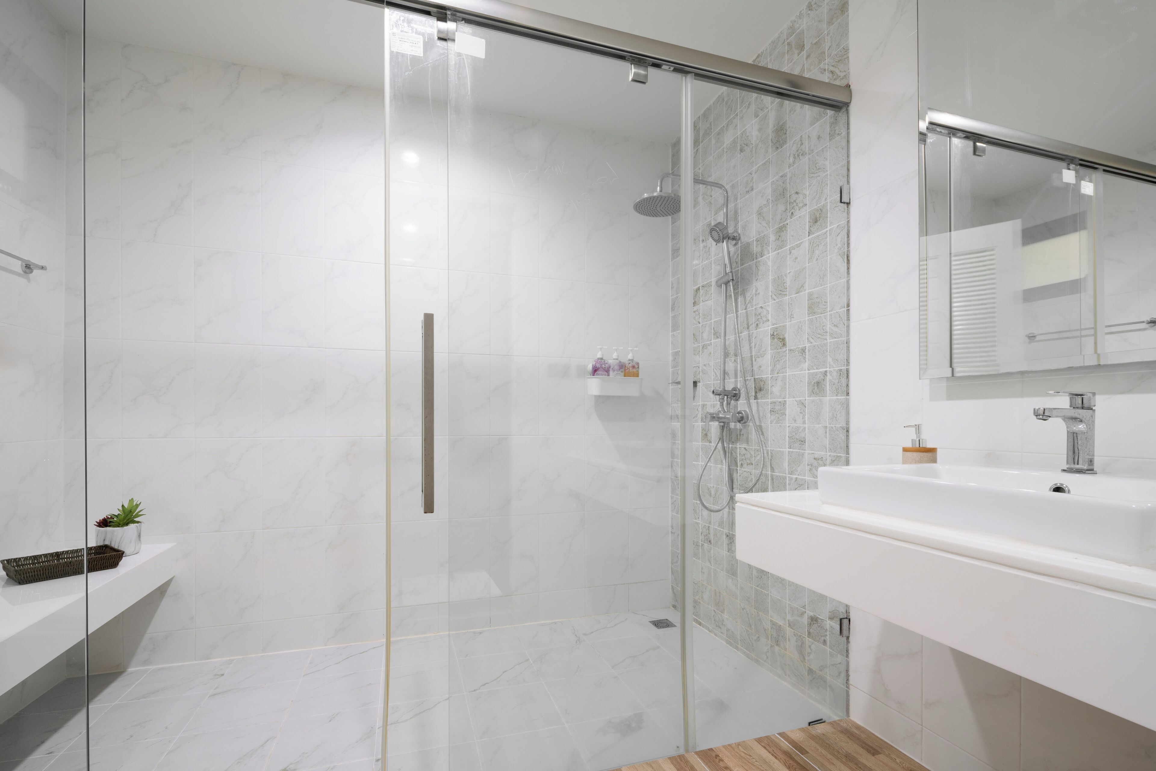 A modern bathroom with a glass-enclosed shower, a white sink, and a wooden floor.