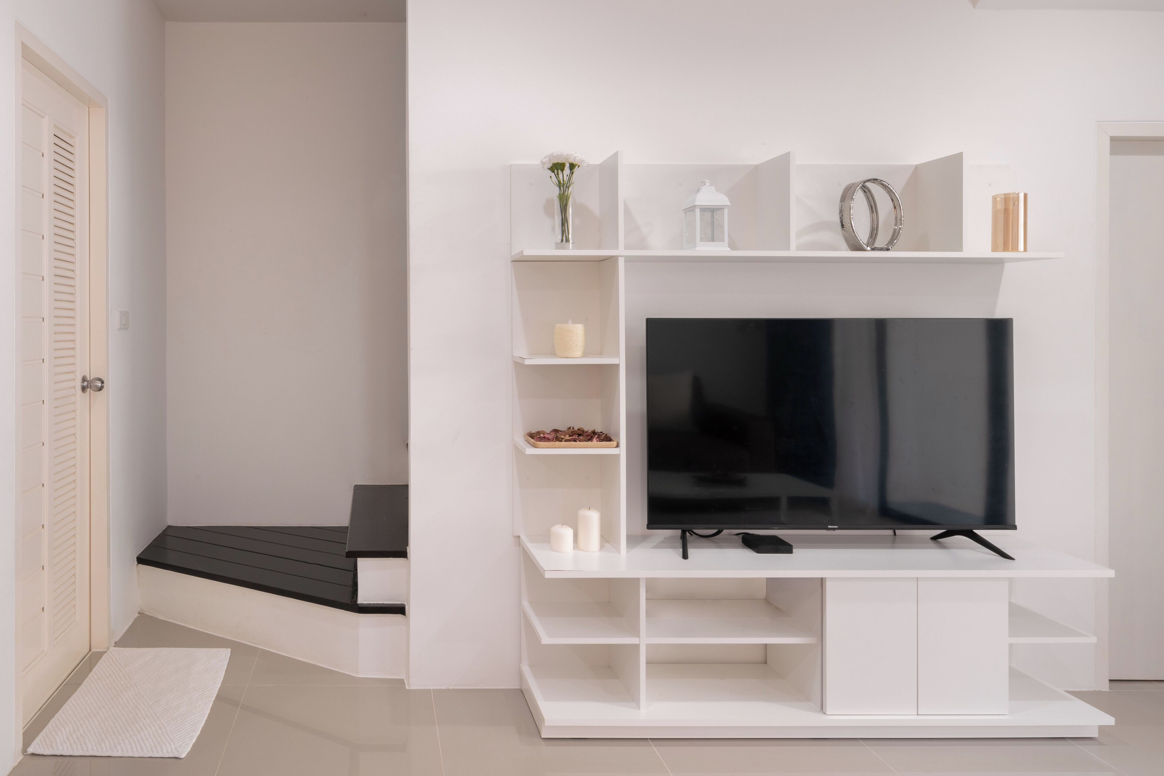 Ein modernes Wohnzimmer mit einem Flachbildfernseher auf einer weißen Unterhaltungsecke, einer kleinen Sitzecke und einer Tür mit Klappläden.
