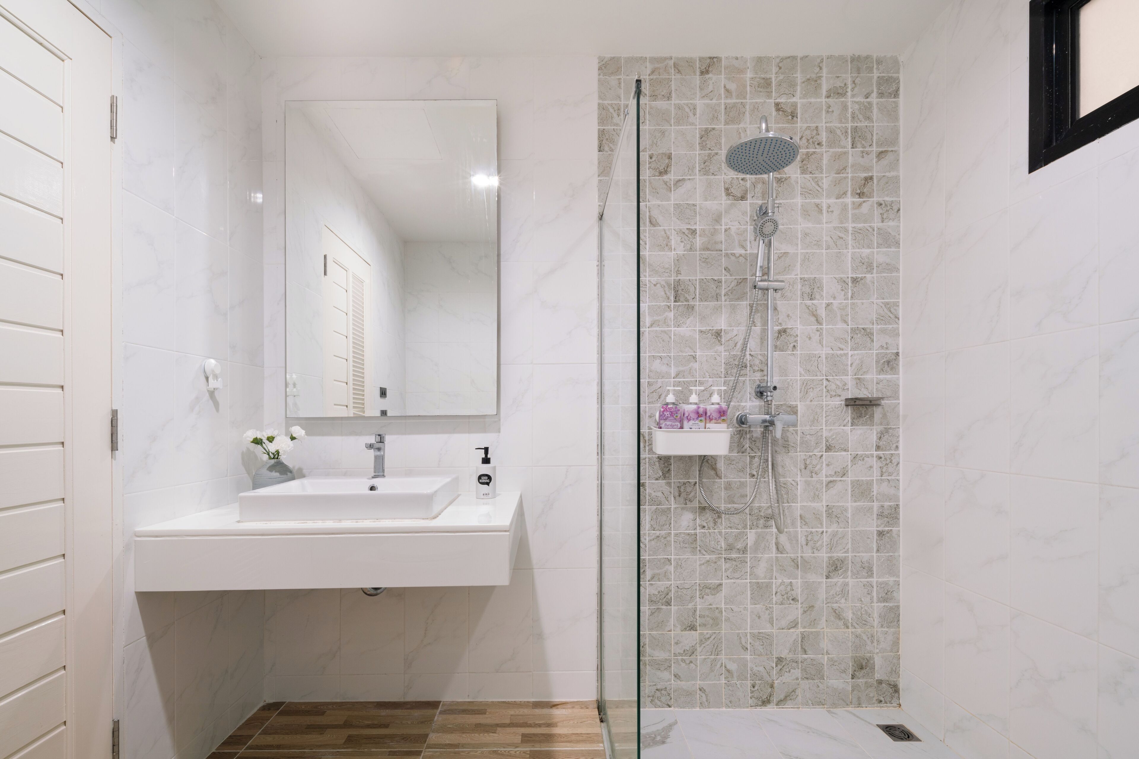 A bathroom with a white sink, mirror, and shower with a tiled wall.