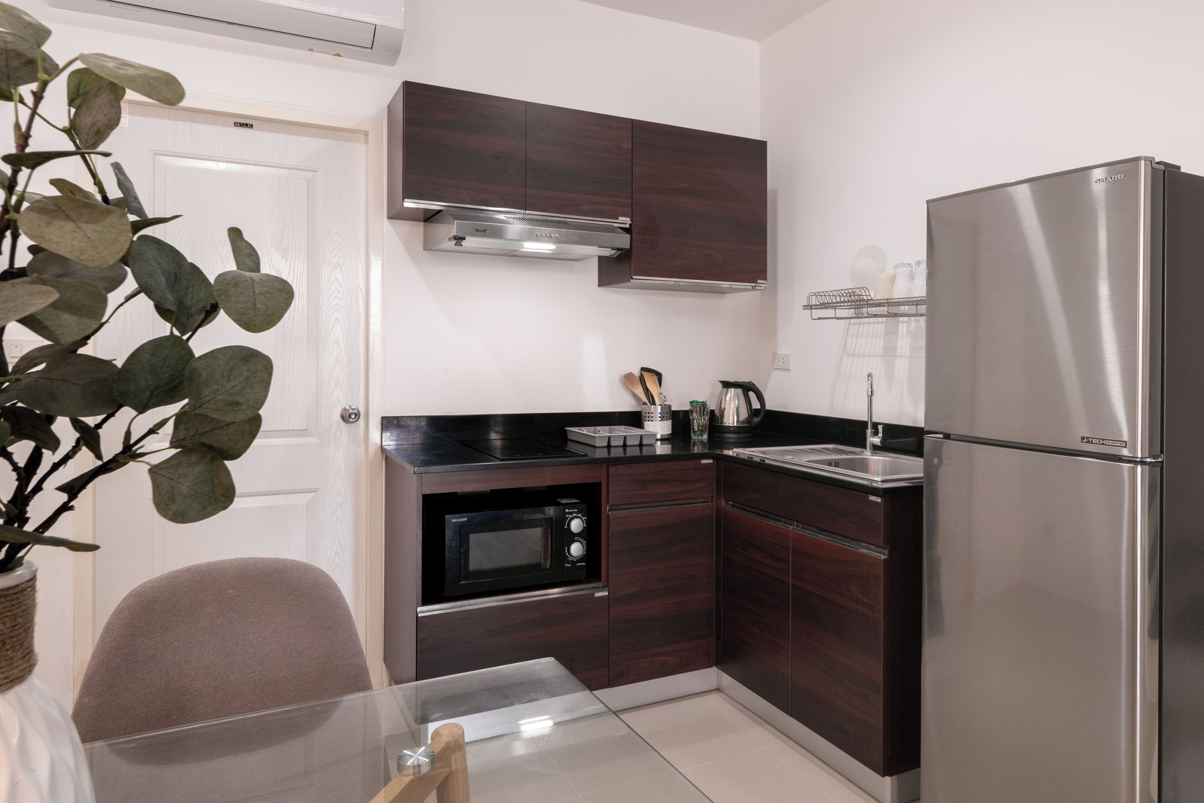 A compact kitchen with dark wood cabinets, a stainless steel refrigerator, a microwave, and a sink.