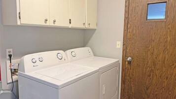 Une buanderie équipée d’un lave-linge et d’un sèche-linge à chargement frontal, de placards en bois au-dessus et d’une porte en bois avec une petite fenêtre.