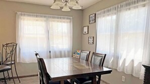 A dining area with a rectangular table and six chairs, large windows with sheer curtains, and a chandelier. - Spacious Home Away From Home! (Bismarck)