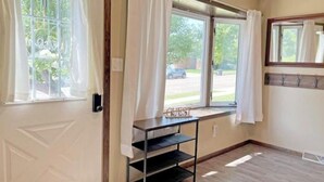 A room with a door, two windows with curtains, a shelf, and a view of the outside. - Spacious Home Away From Home! (Bismarck)