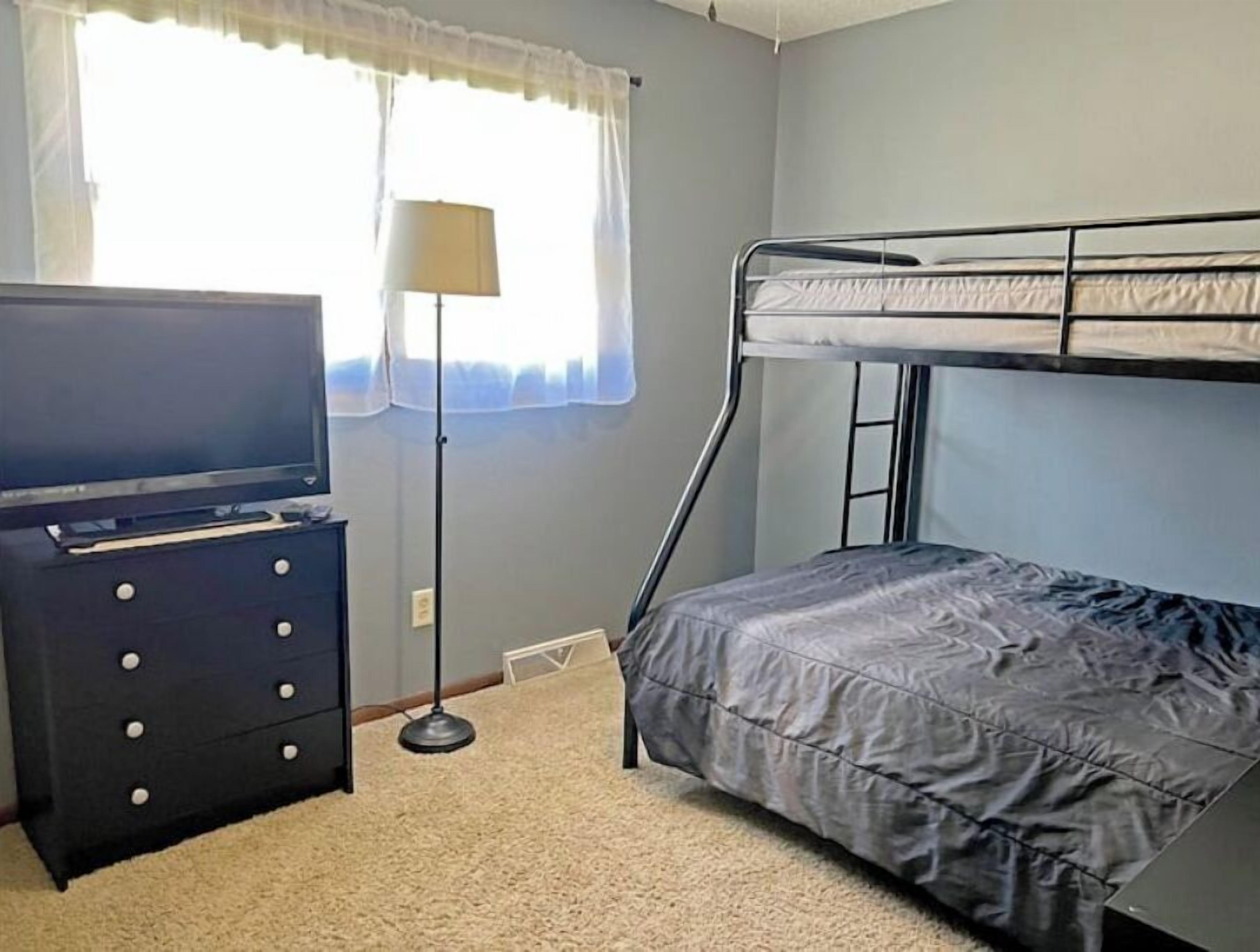 Un lit superposé avec un matelas, une commode avec des tiroirs, une lampe et une fenêtre avec des rideaux.