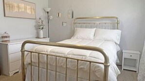 A bedroom with a bed, bedside tables, a dresser, and a wall-mounted light fixture. - Spacious Home Away From Home! (Bismarck)