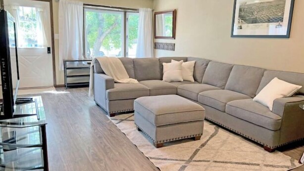A living room with a sectional sofa, ottoman, and a glass coffee table. - Spacious Home Away From Home! (Bismarck)