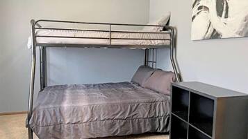 A bunk bed with a grey mattress and pillows, a black TV stand, and a painting on the wall.