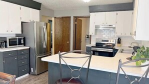 A modern kitchen with stainless steel appliances, a central island with bar stools, and a wooden door in the background. - Spacious Home Away From Home! (Bismarck)