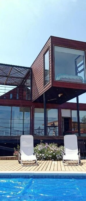 Edifici modern de dues plantes amb zona de piscina, incloent relaxants gandules i vista a la piscina.