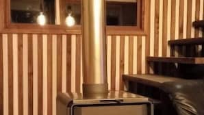 Una estufa de leña con chimenea, una ventana y espacio para almacenar leña.