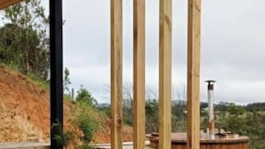 Una terraza de madera con una estructura de pérgola, una pequeña planta en maceta y una gran fuente cilíndrica.
