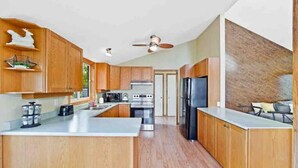 A modern kitchen with wooden cabinets, a central island, stainless steel appliances, and a ceiling fan. - Cozy Cottage by Lake Simcoe | Private Dock & Kayaks Included (Brechin)