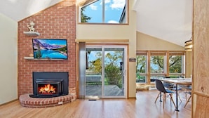 A modern living room with a fireplace, a TV, and a dining area with a view of the outdoors. - Cozy Cottage by Lake Simcoe | Private Dock & Kayaks Included (Brechin)