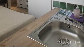 Una pequeña cocina americana con un lavabo, un taburete de madera, un globo terráqueo y un armario blanco.