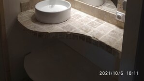 Un baño con un lavamanos redondo, un espejo y un revestimiento de azulejos.