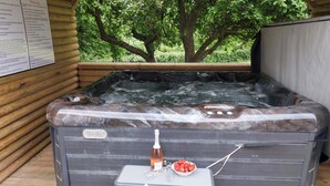 A hot tub with a wooden deck, a small table with a bottle and strawberries, and a sign on the wall. - Hazelgarth House (Filey)
