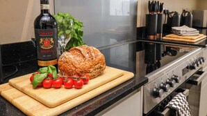 A modern kitchen with a stainless steel stove, a cutting board with bread, tomatoes, and basil, and a bottle of Chianti wine. - Hazelgarth House (Filey)