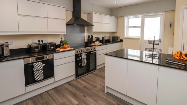 A modern kitchen with white cabinets, a black stove, and a window providing natural light. - Hazelgarth House (Filey)