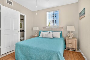 A bedroom with a bed, two bedside tables, a nightstand, a window, and a door. - Beach Access | Lanai | Kayak & Boat Rentals (Fort Myers Beach)