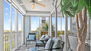 A sunlit balcony with a ceiling fan, a dining table with chairs, and a sofa with cushions. - Gulf-View Lanai | FMB Condo | Pets OK (Fort Myers Beach)