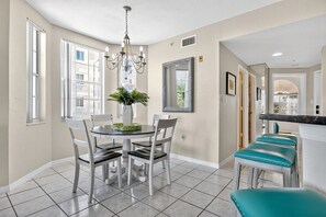 A dining area with a round table, white chairs, a chandelier, and a mirror on the wall.