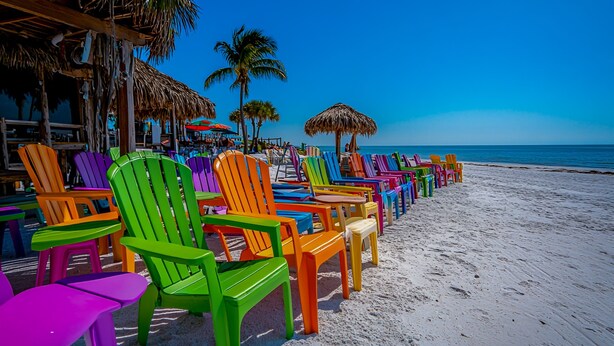 A beach with colorful chairs lined up and thatched umbrellas. - Gulf-View Lanai | FMB Condo | Pets OK (Fort Myers Beach)