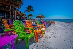 A beach with colorful chairs lined up and thatched umbrellas. - FMB Condo | Near Times Square | Pets OK (Fort Myers Beach)
