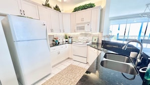 A modern kitchen with white cabinets, a stainless steel refrigerator, a microwave, and a sink. - Gulf-View Lanai | FMB Condo | Pets OK (Fort Myers Beach)