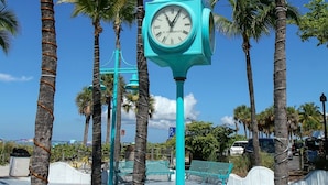A turquoise clock post surrounded by palm trees in a sunny outdoor setting. - Gulf-View Lanai | FMB Condo | Pets OK (Fort Myers Beach)