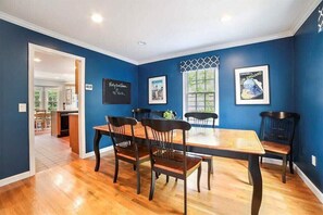 A dining room with a wooden table and chairs, blue walls, and a window with a view.