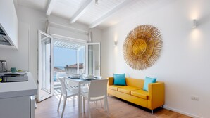 Un salón luminoso con un sofá amarillo, una mesa de comedor con sillas y un gran elemento decorativo en la pared.