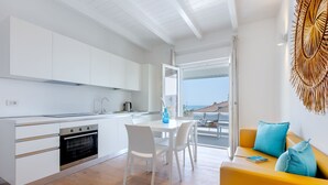 Una cocina moderna con armarios blancos, un comedor con mesa y sillas, y un sofá amarillo con cojines azules.