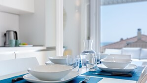 Mesa de comedor servida con cuencos, platos, vasos y cubiertos blancos, con vista a un edificio a través de una ventana.