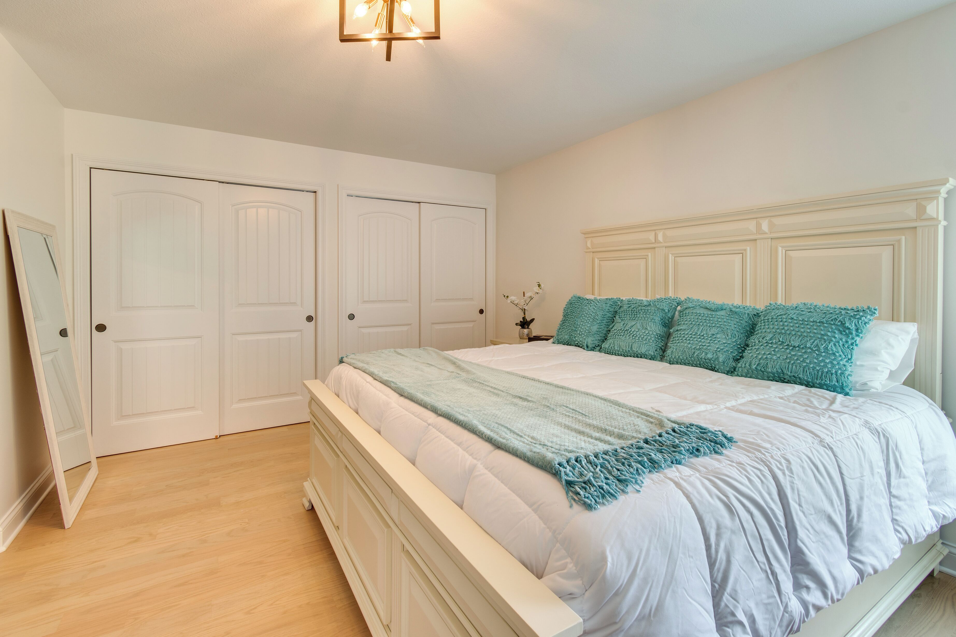Une chambre à coucher avec un lit blanc, des oreillers turquoise et une tête de lit blanche.
