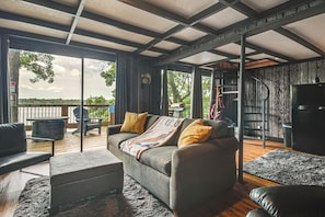 A modern living room with a sofa, a coffee table, and a fireplace. There is a balcony with a view of the outdoors. - Private Hot Tub & Dock: Lakefront Grove Retreat! (Grove)