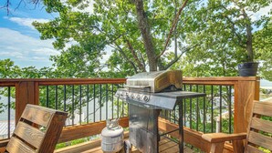 Eine Holzterrasse mit Grill, Propangasflasche und einer Bank.