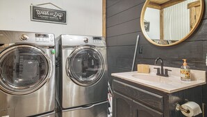 Ein Waschraum mit zwei Edelstahl-Waschmaschinen mit Frontlader, einem Waschbecken mit Spiegel darüber und einem Schild, das Self-Service-Waschmöglichkeiten anzeigt.