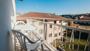 Ein Balkon mit weißen Stühlen und einem Tisch, mit Blick auf eine Wohngegend mit Terrakotta-Dächern.