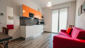 Eine moderne Küche mit weißen und orangefarbenen Schränken, einem roten Sofa und einem Esstisch.