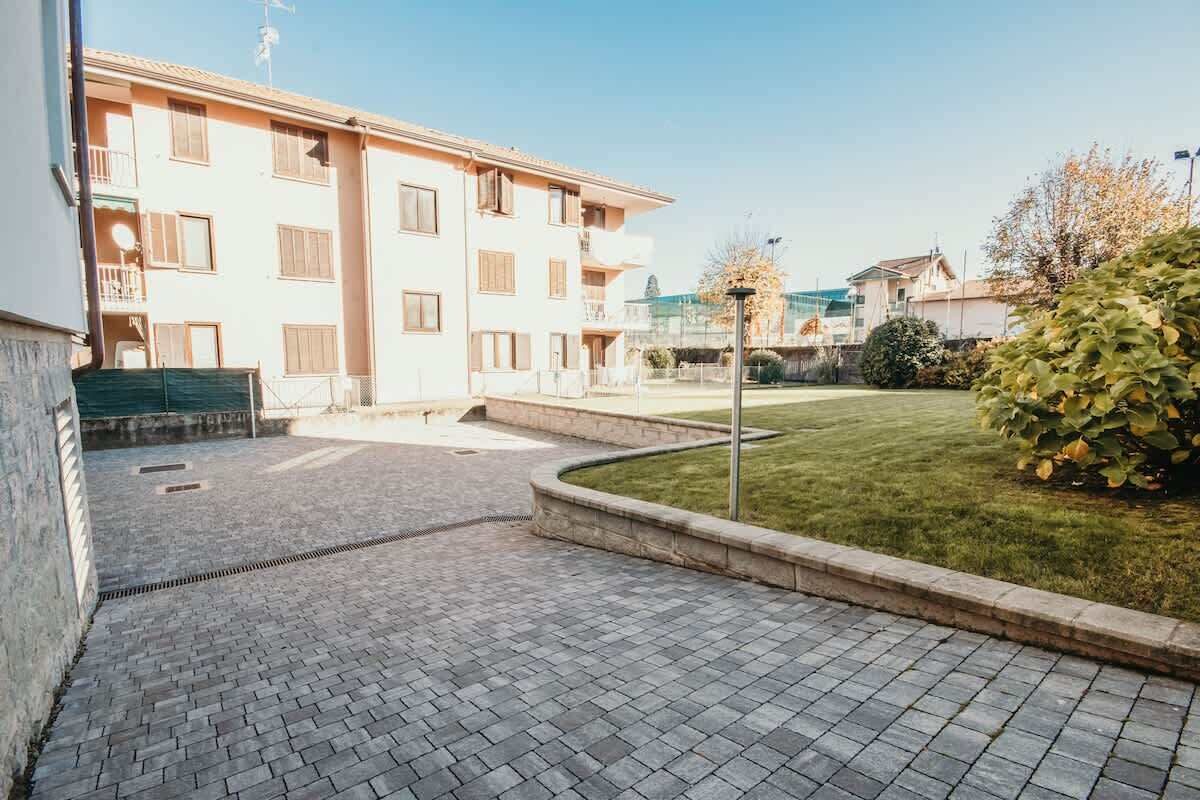 Um pátio com área pavimentada, gramado e um edifício com várias andares e varandas.