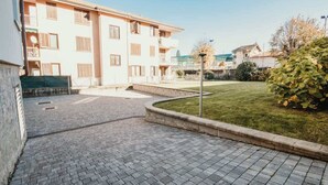 Un patio con suelo empedrado, césped y un edificio de varios pisos con balcones.