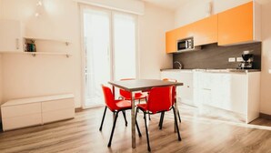Una cocina moderna con armarios blancos, microondas y cafetera. Cuenta con un comedor con mesa de madera y sillas rojas.