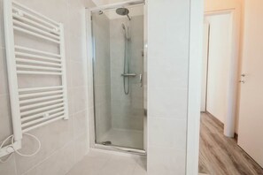 Een douche met glazen wand, een handdouche en een wandrek voor handdoeken.